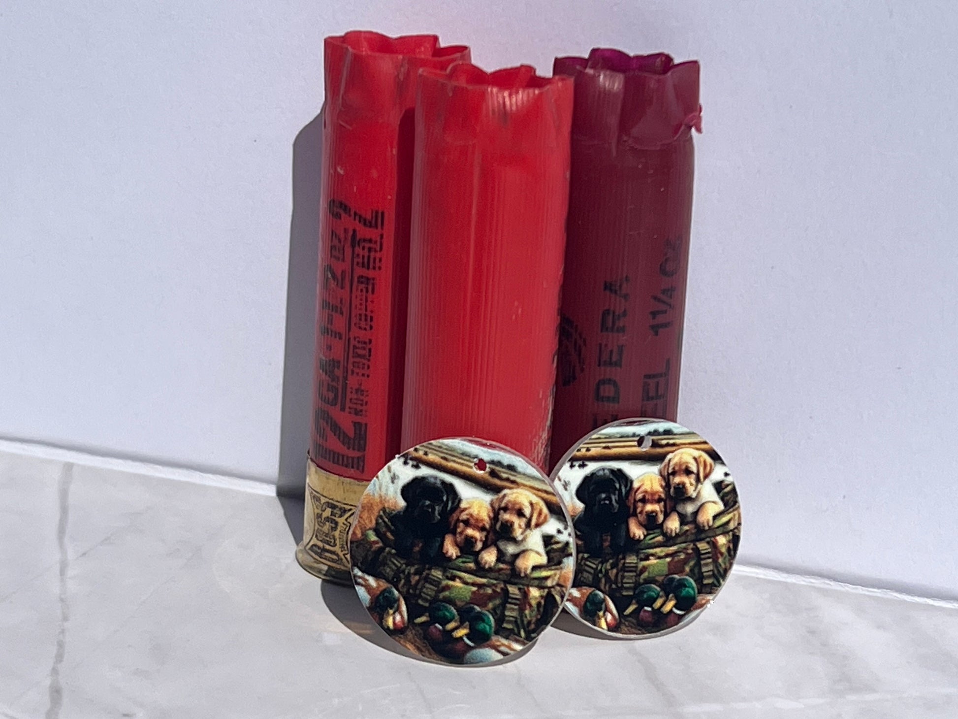 Two red shotgun shells with decorative bases featuring earrings with puppies on a white surface.