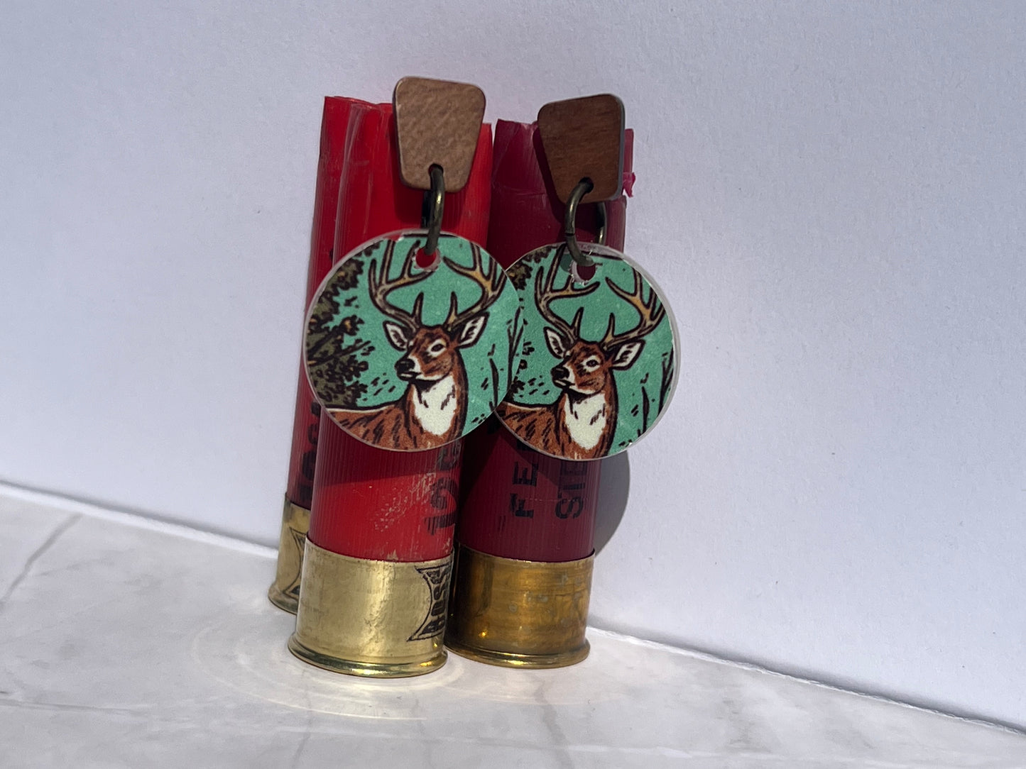 Deer-themed earrings with wood post displayed on red shotgun shells against a white background