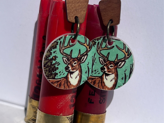Deer-themed earrings with wood post displayed on red shotgun shells against a white background
