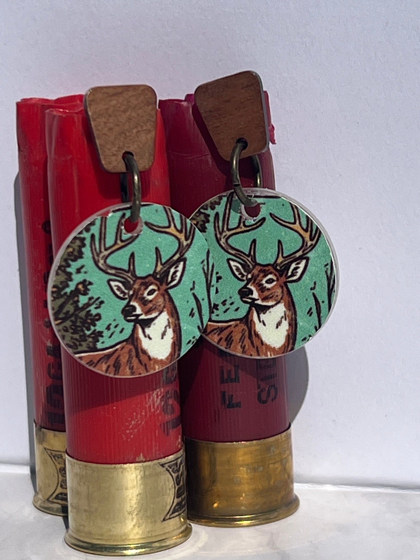 Deer-themed earrings with wood post displayed on red shotgun shells against a white background
